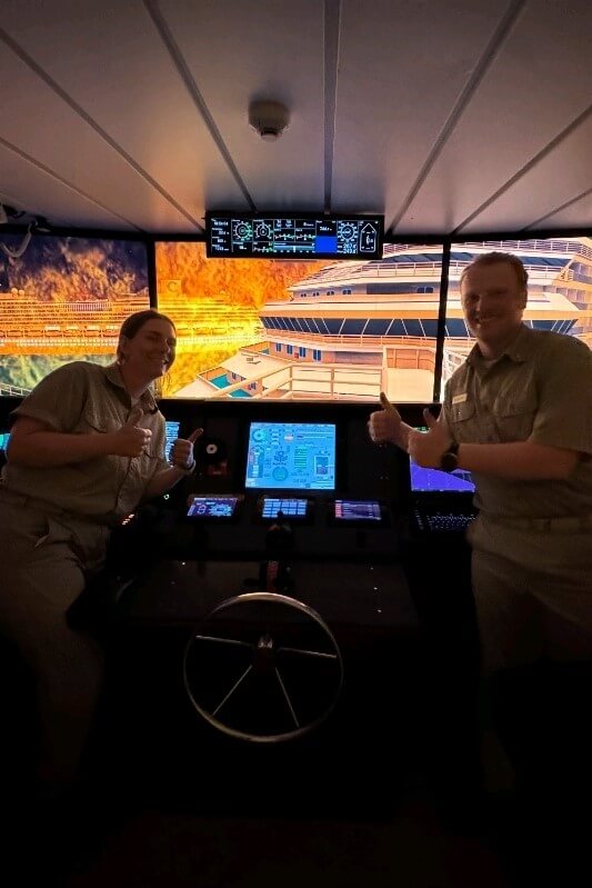 two cadets giving thumbs up in front of simulator with image of flames