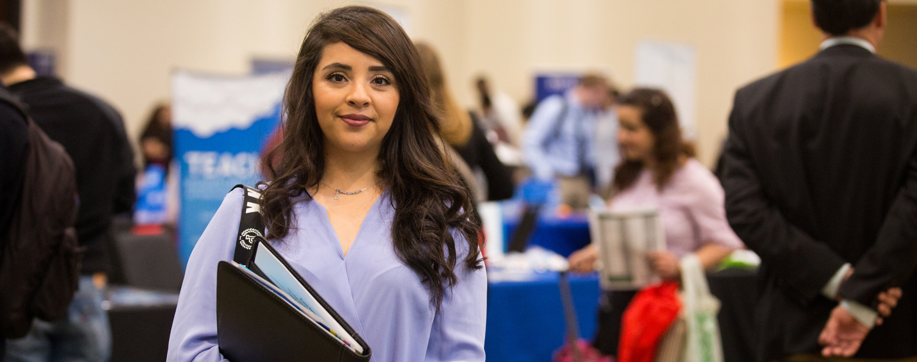 Career Services Hero Image - Nicely dressed woman looking into camera, conference tables out of focus in the background