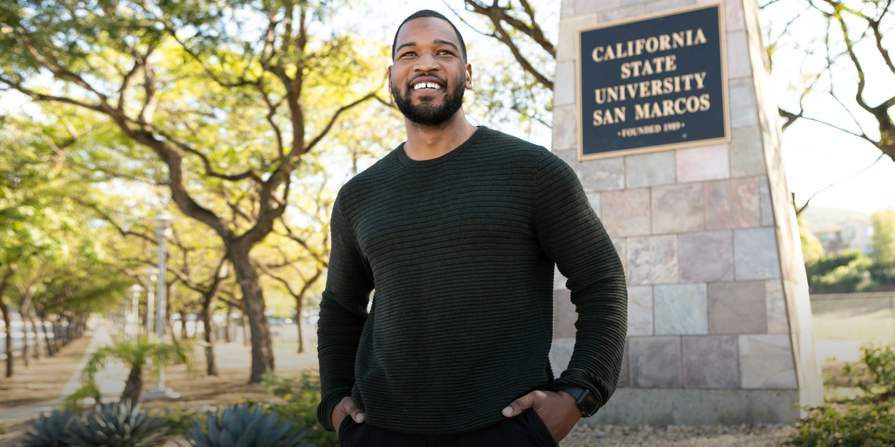 Louis stands in front of a CSU San Marcos sign.