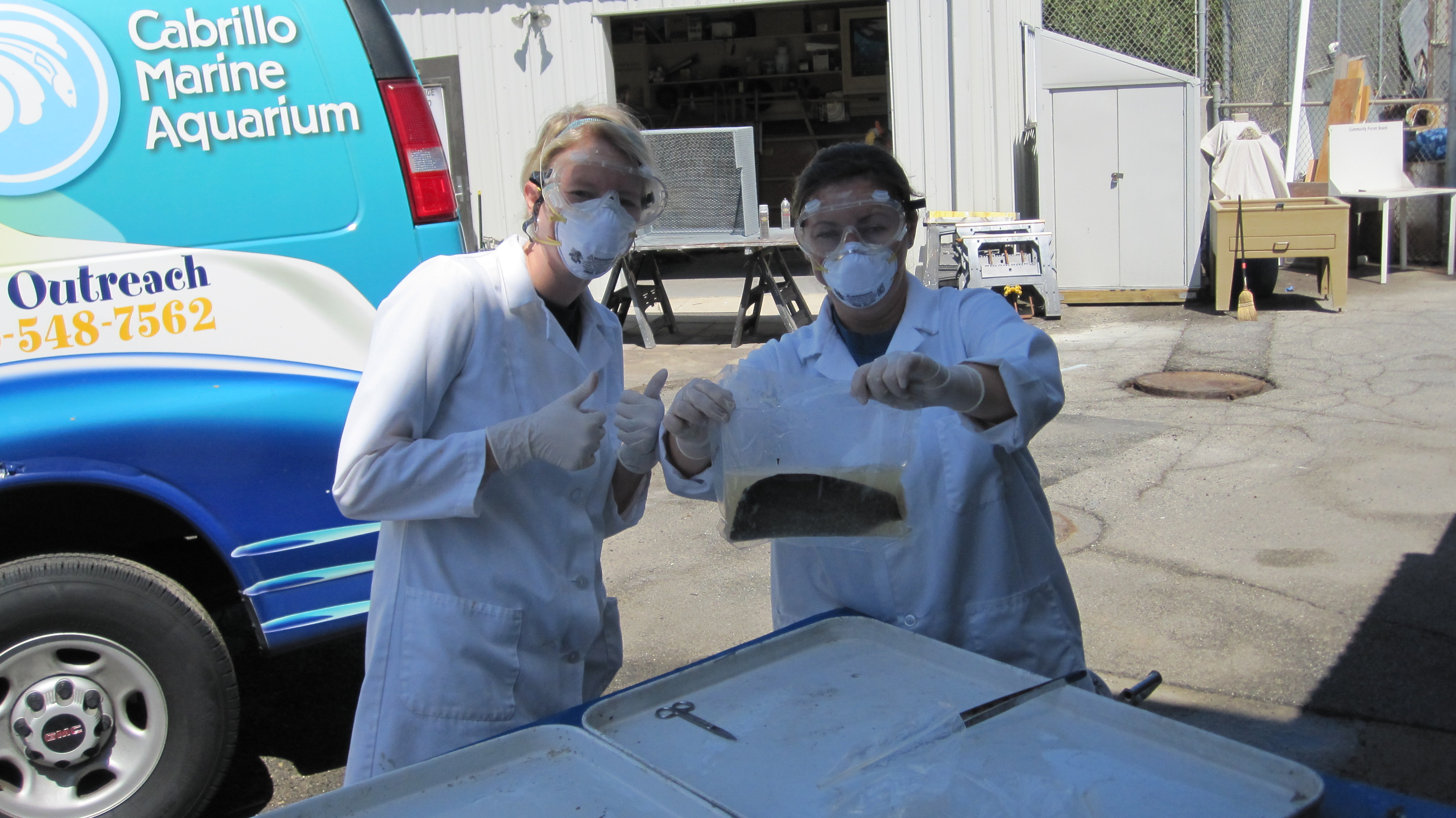 Three students in white lab coats and rubber gloves looking at jar 
