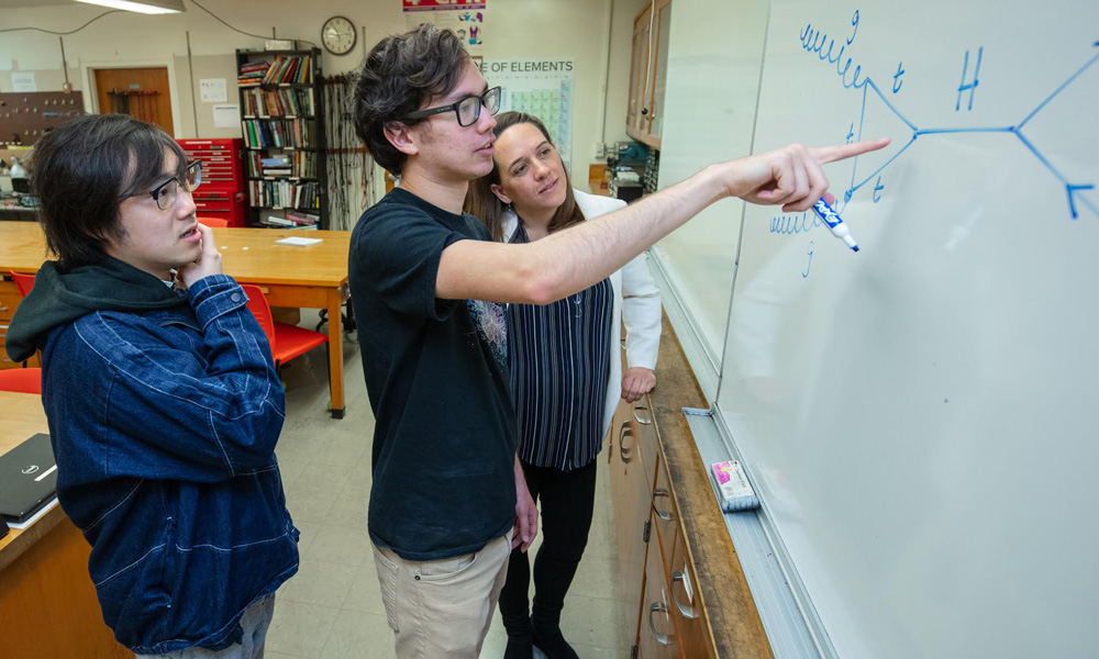 Three Cal State East Bay Students looking at a dry erase board