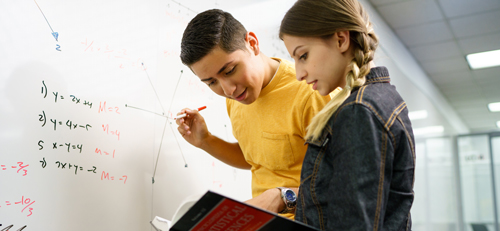 students looking in a book, math equations on whiteboard
